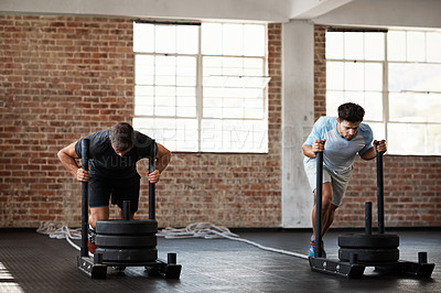 Buy stock photo Shot of two men in a crossfit class pushing weights across the floor