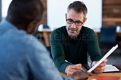 Buy stock photo Shot of two male coworkers discussing paperwork at a desk in an office