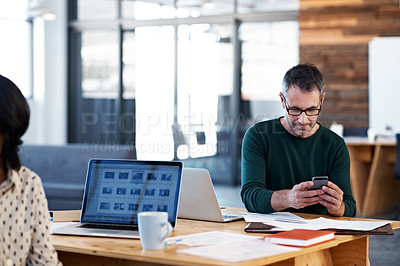 Buy stock photo Shot of an office worker text messaging while sitting at his desk