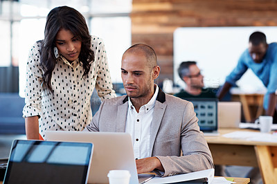 Buy stock photo Shot of two coworkers talking together over a laptop at a desk in an office