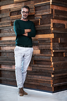 Buy stock photo Portrait of a handsome businessman leaning against a wall in an office