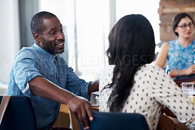 Buy stock photo Shot of two coworkers talking together while sitting at a table in an office