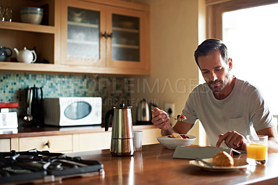 Buy stock photo Cropped shot of a handsome man eating breakfast while using a tablet