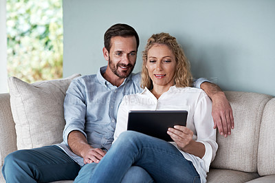 Buy stock photo Cropped shot of a couple using a tablet while relaxing on the sofa