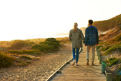 Buy stock photo Rearview shot of an affectionate couple walking hand-in-hand outdoors