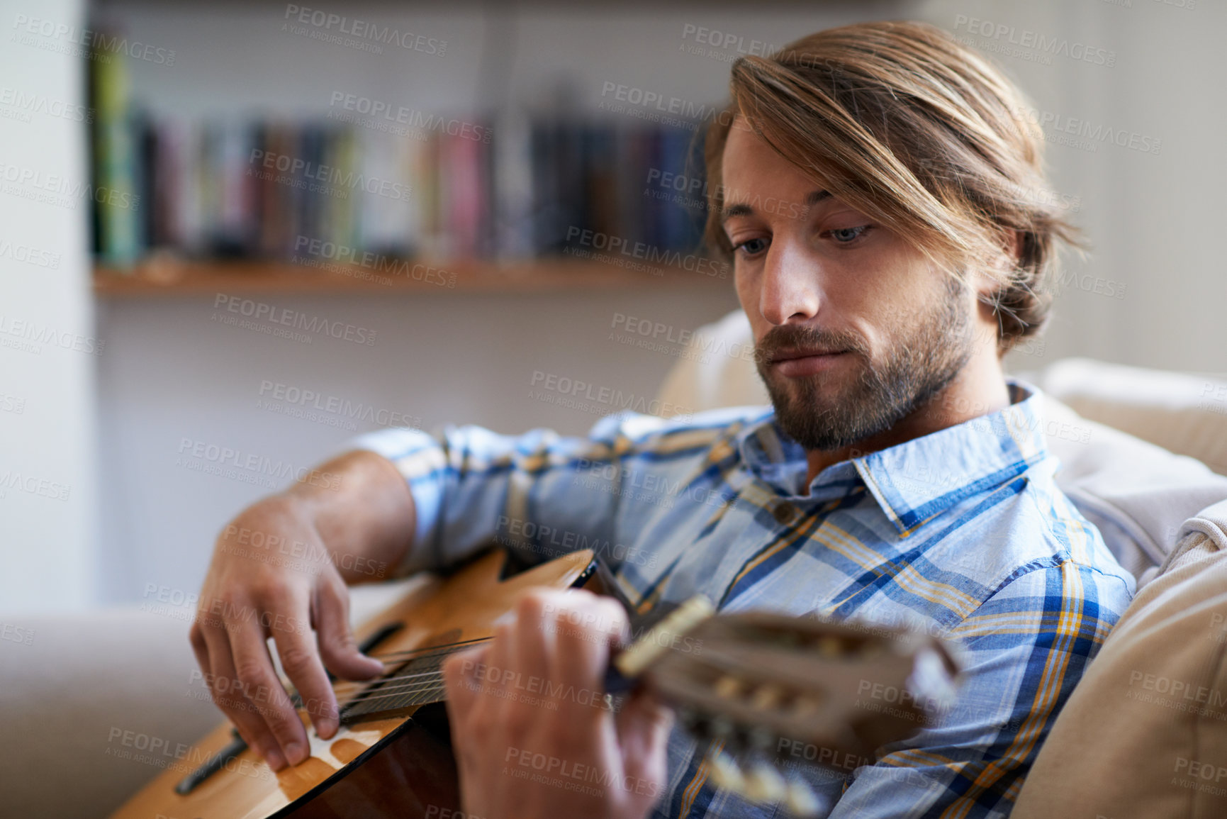 Buy stock photo Couch, man and play guitar for music, practice strumming and talent performance on weekend. Home, person and musician with acoustic string instrument for creative skill, audio and rhythm at apartment