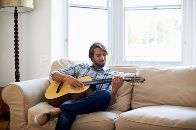 Buy stock photo Shot of a young man playing a guitar while relaxing at home