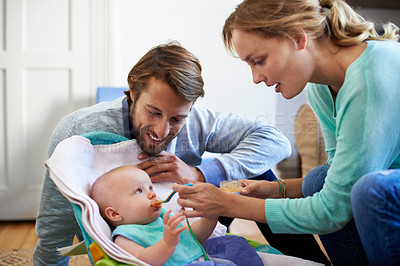 Buy stock photo Shot of a young couple feeding their baby at home