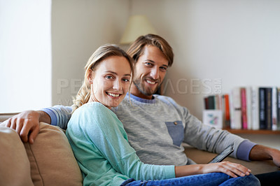 Buy stock photo Portrait of a young couple using a digital tablet while relaxing on a sofa at home
