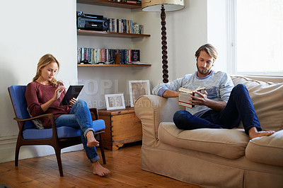 Buy stock photo Shot of a young couple relaxing with a book and digital tablet in the living room