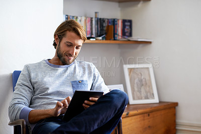 Buy stock photo Shot of a young man using a digital tablet while relaxing at home