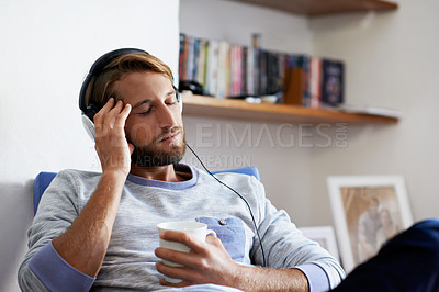 Buy stock photo Shot of a young man relaxing at home listening to music