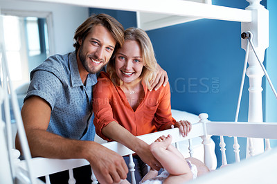 Buy stock photo Portrait of a young couple standing beside their baby in a crib