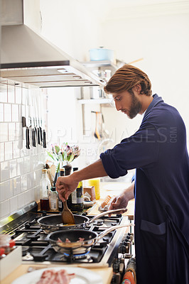 Buy stock photo Shot of a young man cooking breakfast in the kitchen