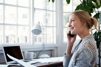 Buy stock photo Shot of a young woman talking on the phone while working on a laptop at home
