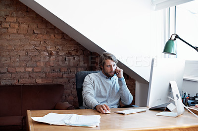 Buy stock photo Shot of a young man talking on the phone while working on a computer at home