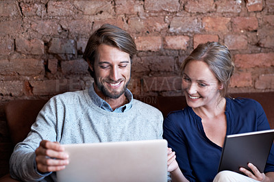 Buy stock photo Shot of a young couple using a digital tablet and laptop while relaxing at home
