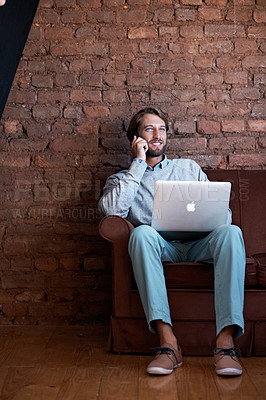 Buy stock photo Shot of a young man talking on his cellphone and using a laptop while sitting at home