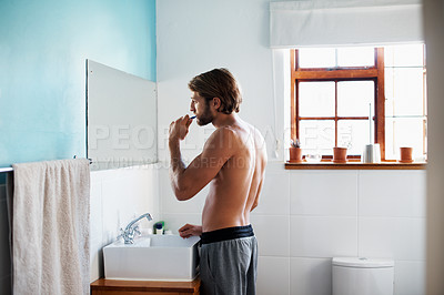 Buy stock photo Shot of a young man brushing his teeth in the bathroom in the morning