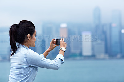 Buy stock photo Shot of a young asian woman taking a picture of the Hong Kong skyline