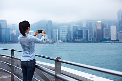 Buy stock photo Rearview shot of a young woman taking a picture of the Hong Kong skyline