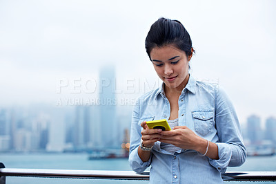 Buy stock photo Shot of an attractive woman holding a smartphone in front of the Hong Kong skyline