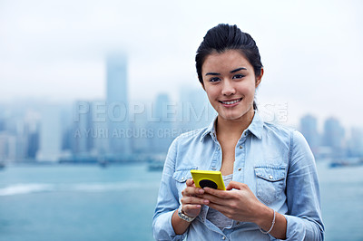 Buy stock photo Portrait of an attractive woman holding a smartphone in front of the Hong Kong skyline