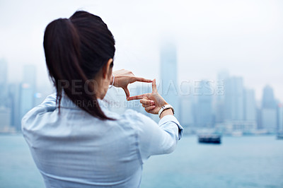 Buy stock photo Rearview shot of a young woman framing the Hong Kong skyline with her fingers