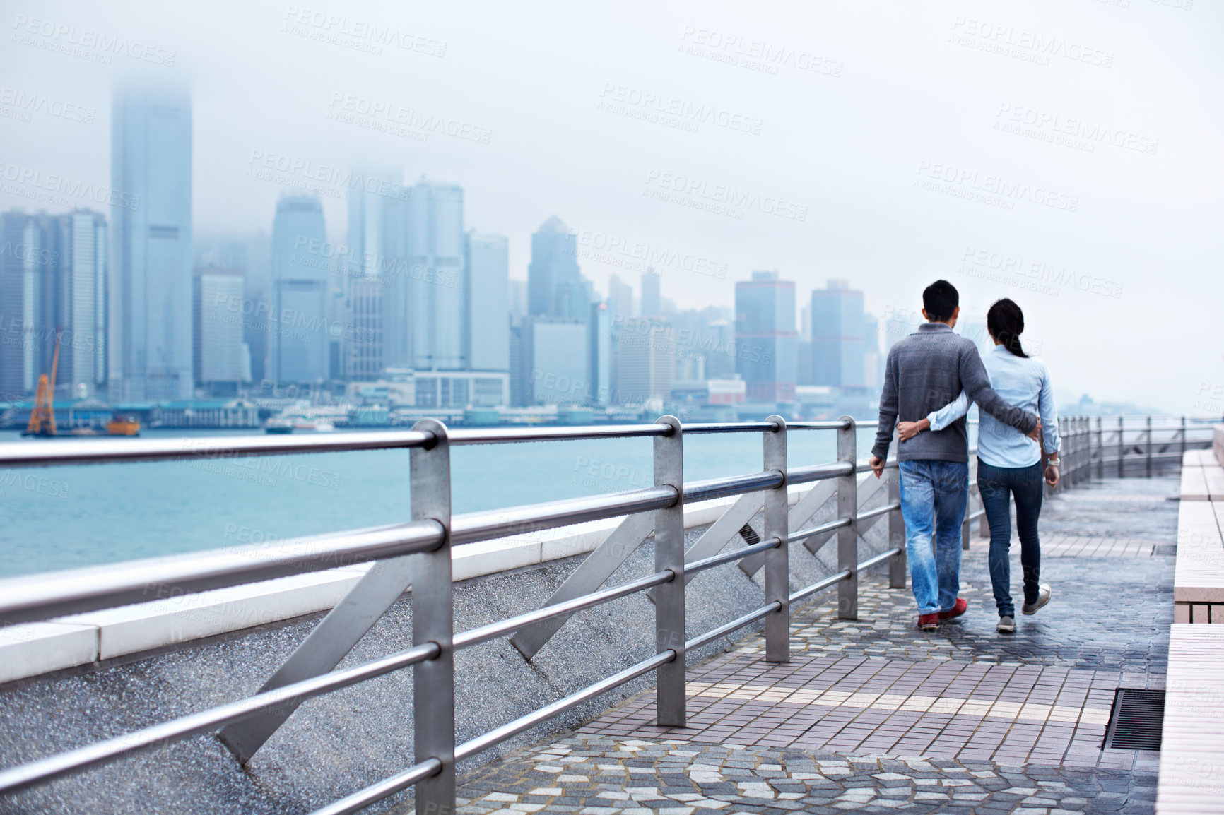 Buy stock photo Bridge, walking and back of couple at waterfront for bonding, connection and sightseeing together. Hug, city and man with woman outdoor for love, tourism or explore on holiday, vacation and weekend