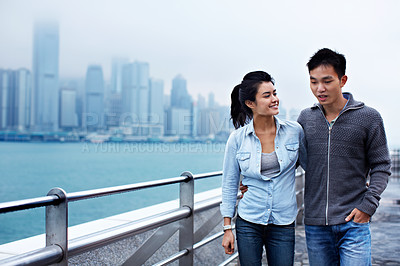 Buy stock photo Shot of a young asian couple walking along the Hong Kong waterfront