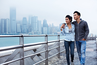 Buy stock photo Shot of a young asian couple walking along the Hong Kong waterfront