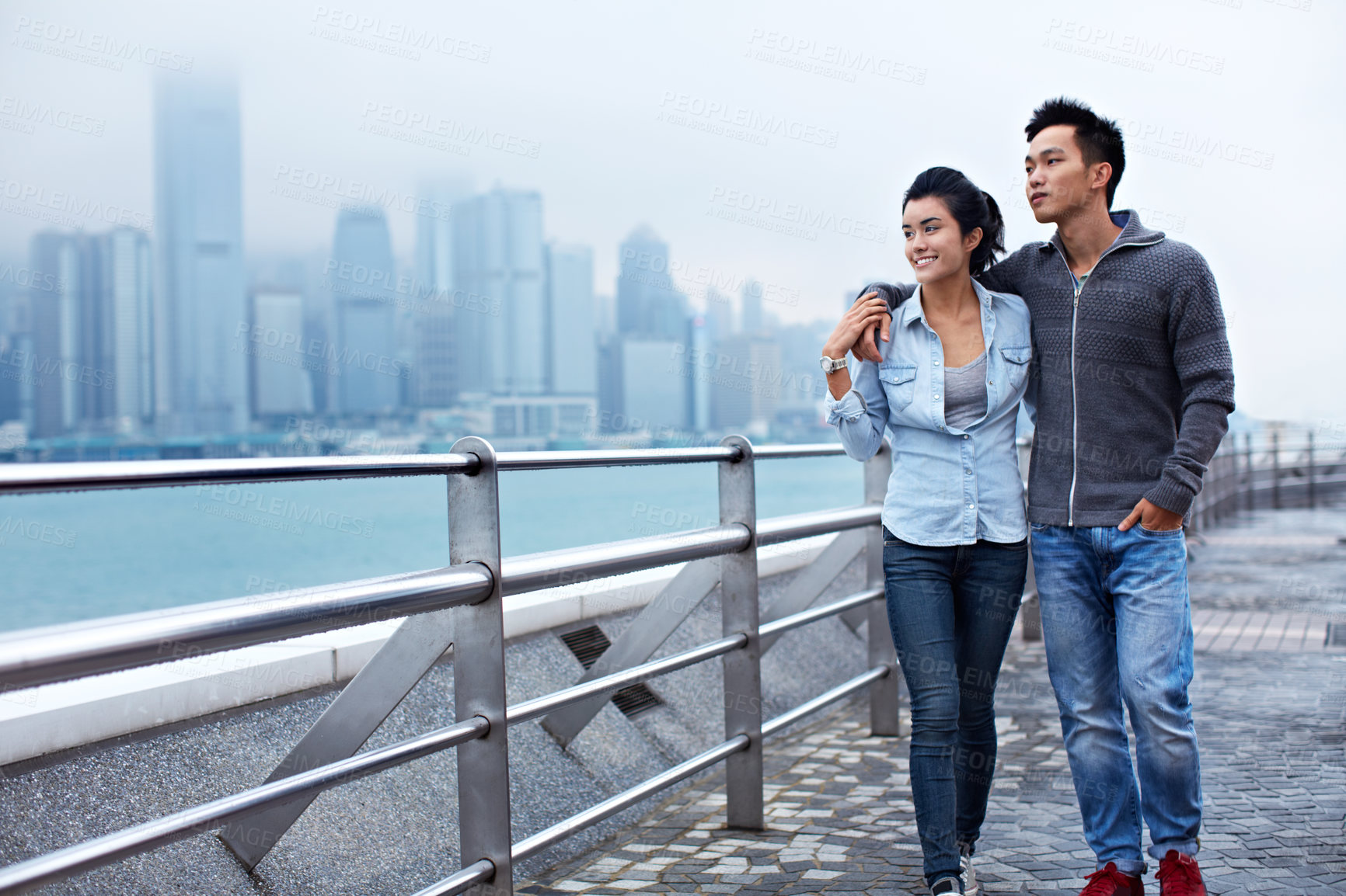 Buy stock photo Shot of a young asian couple walking along the Hong Kong waterfront
