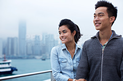 Buy stock photo Shot of a young asian couple walking along the Hong Kong waterfront