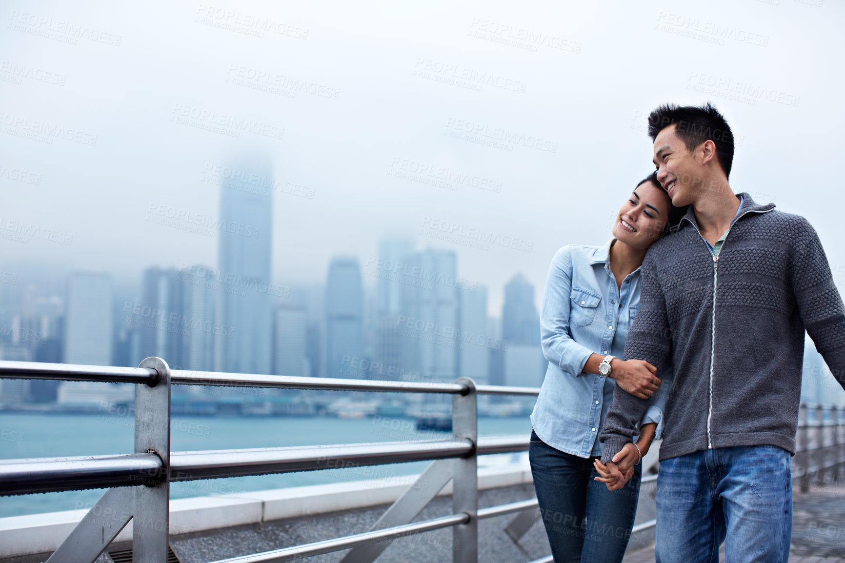 Buy stock photo Shot of a young asian couple walking along the Hong Kong waterfront