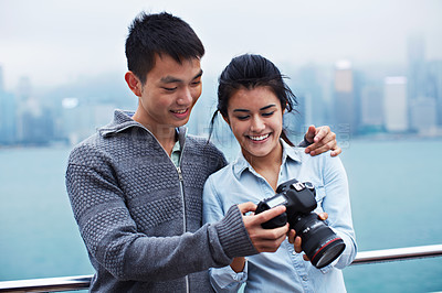 Buy stock photo Shot of a young couple looking at photos on a digital slr in front of the Hong Kong skyline