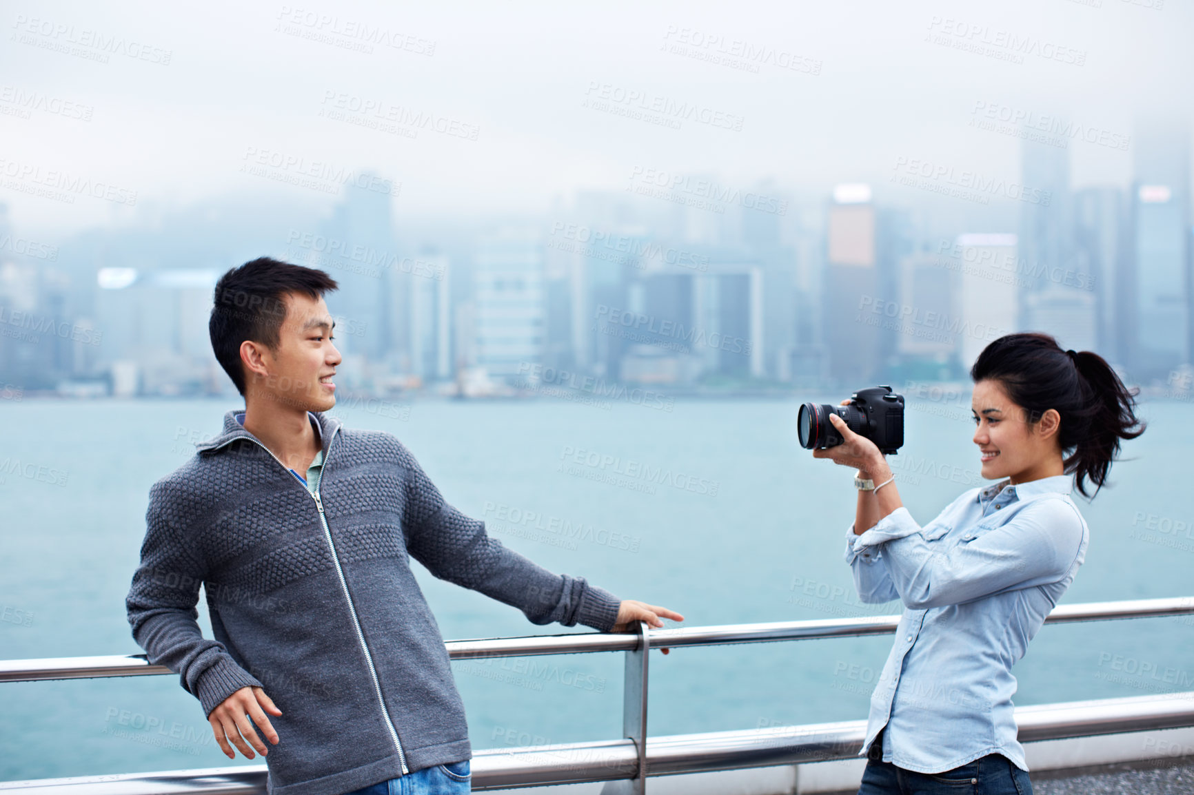 Buy stock photo Shot of a young couple taking photos of each other in front of the Hong Kong skyline