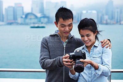 Buy stock photo Shot of a young couple looking at photos on a digital slr in front of the Hong Kong skyline