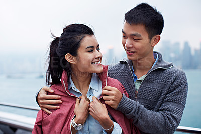 Buy stock photo Shot of a young man putting his jacket over his girlfriend's shoulders while walking along the Hong Kong waterfront