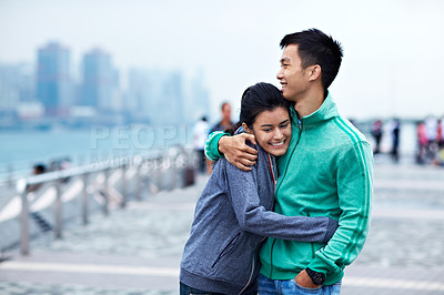 Buy stock photo Shot of an affectionate young asian couple hugging while walking along the Hong Kong waterfront