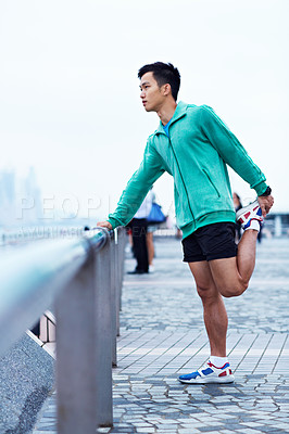 Buy stock photo Shot of a young asian man warming up for a jog along the Hong Kong skyline
