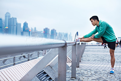 Buy stock photo Shot of a young asian man warming up for a jog along the Hong Kong skyline