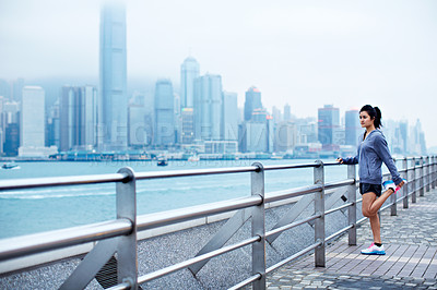 Buy stock photo Full length shot of an attractive young woman stretching before a run along the Hong Kong waterfront