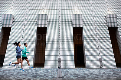 Buy stock photo Full length shot of a young man and woman jogging in front of a building's facade