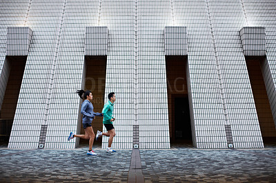 Buy stock photo Full length shot of a young man and woman jogging in front of a building's facade