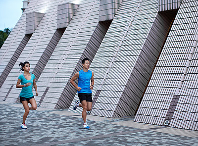 Buy stock photo Full length shot of a young man and woman jogging in front of a building's facade