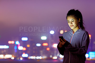 Buy stock photo Shot of an attractive young woman holding a cellphone in front of the Hong Kong skyline at night