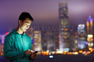 Buy stock photo Shot of a young man holding a cellphone in front of the Hong Kong skyline at night