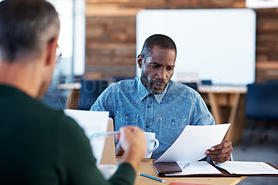 Buy stock photo Shot of two male coworkers discussing paperwork at a desk in an office