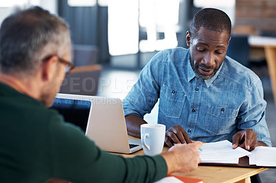 Buy stock photo Shot of two male coworkers discussing paperwork at a desk in an office