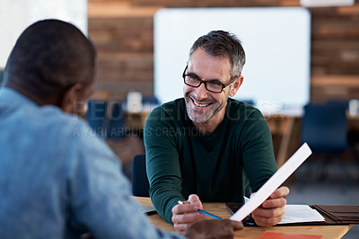 Buy stock photo Shot of two male coworkers discussing paperwork at a desk in an office